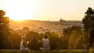 three people sitting on a hill looking at a city at Yellow apartment few steps from metro in Prague