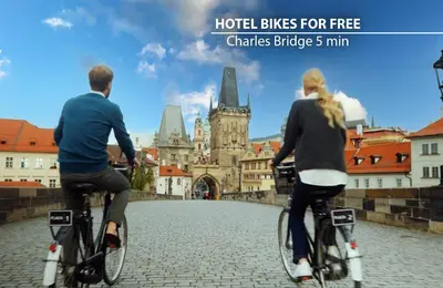 a man and woman riding bikes down a street at Hotel St George - Czech Leading Hotels in Prague
